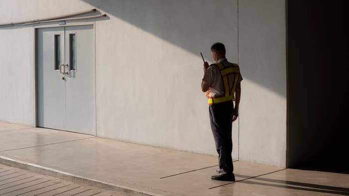 Security guard standing with a walkie-talkie in a minimalist, industrial setting