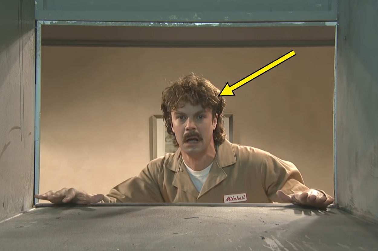 A person with curly hair and a mustache, wearing a uniform, appears surprised through an opening. Arrow pointing at them