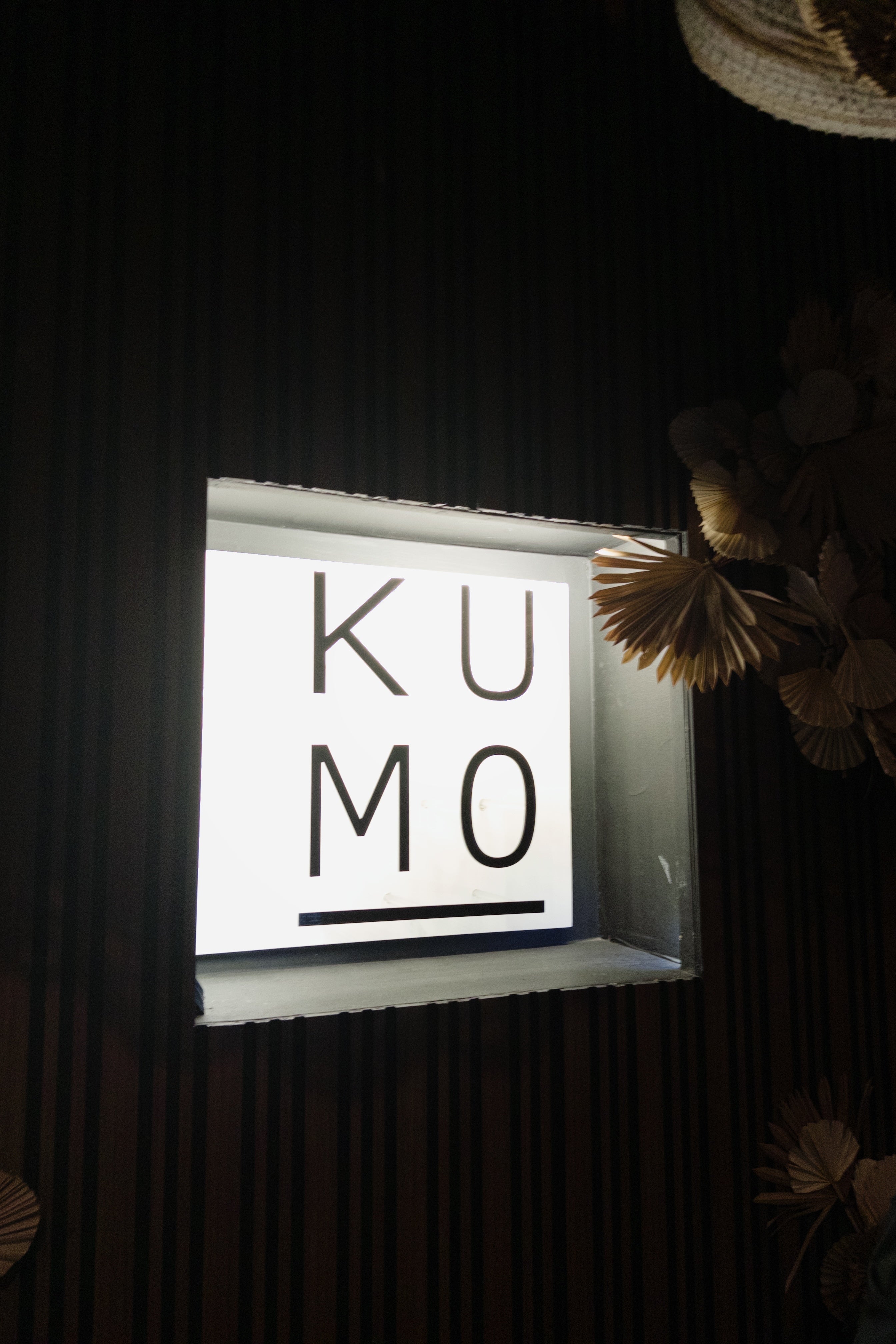 A minimalist illuminated sign reading "KUMO" in bold letters