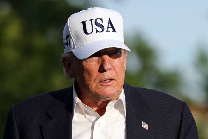 Person wearing a suit jacket and a baseball cap with "USA" text