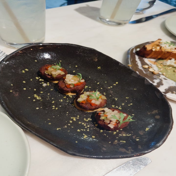 Appetizing dish with bite-sized gourmet appetizers garnished with herbs on a dark oval plate, set on a dining table