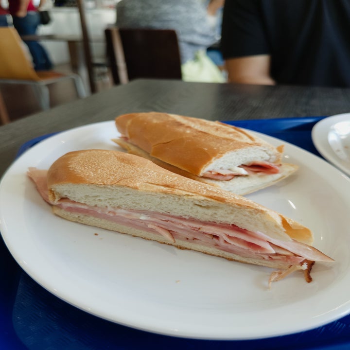 A sandwich with sliced ham layered between a baguette, placed on a white plate