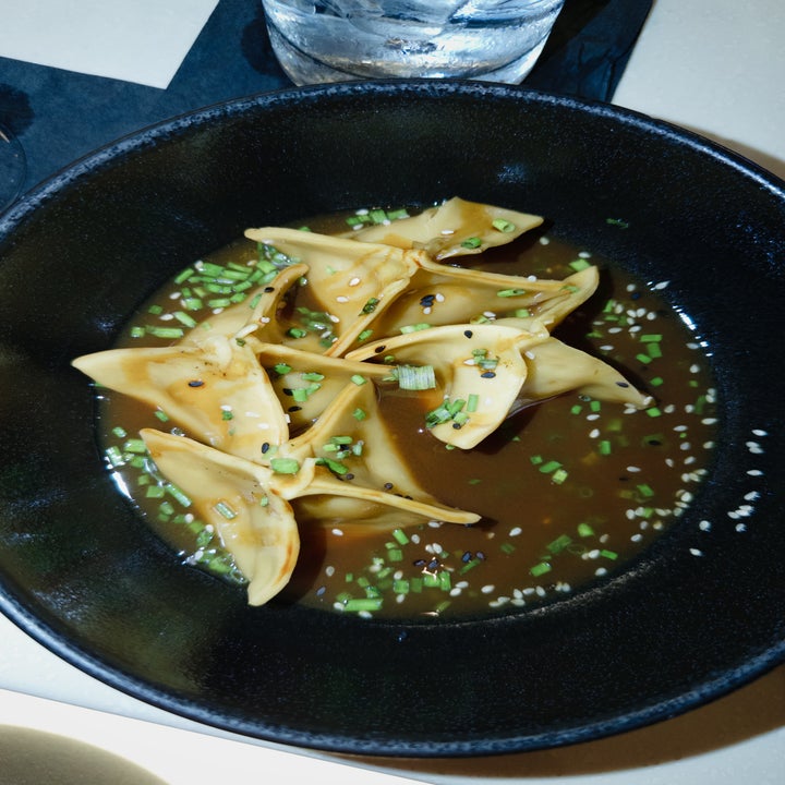 Dumplings in a broth, sprinkled with chives and sesame seeds, served in a black bowl
