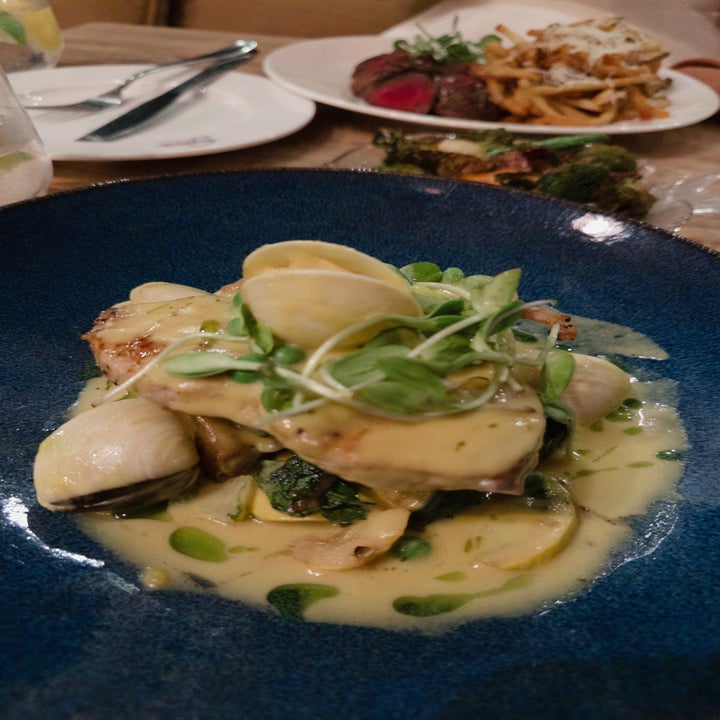 Elegant plated dish with pasta shells, greens, and creamy sauce. In the background, a plate of steak and fries
