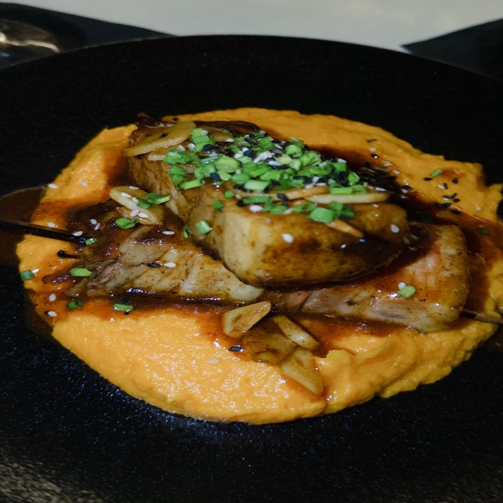 A dish featuring seared meat atop creamy puree, garnished with chopped greens and sliced almonds in a savory sauce