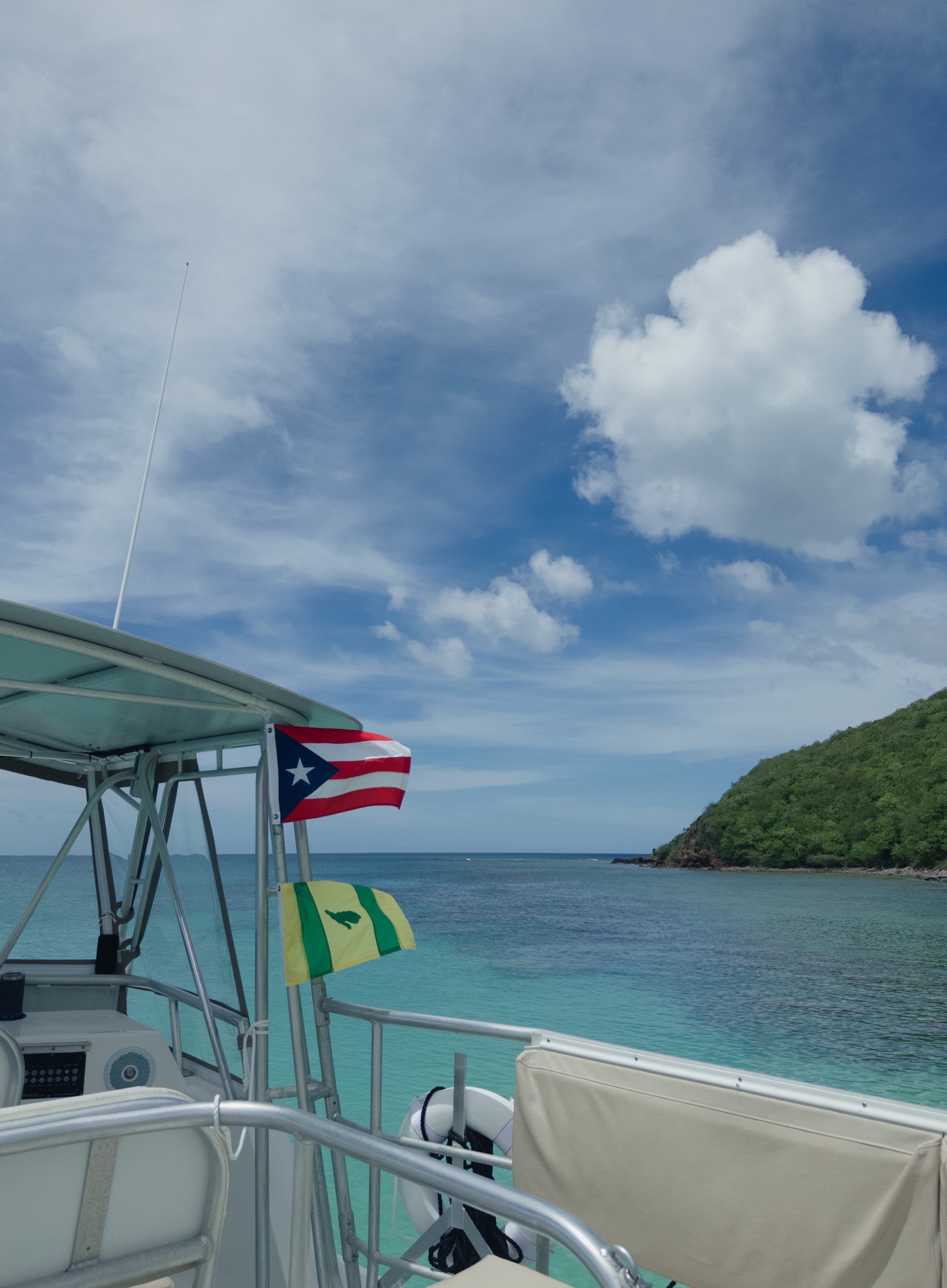 Boat with Puerto Rican and green-yellow flags on a clear beach with lush hillside and open sky