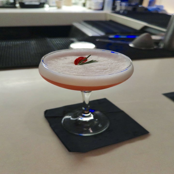 Elegant cocktail in a coupe glass with a foamy top, garnished with a small red flower and a green leaf, on a bar counter with a dark napkin
