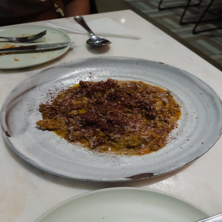 A plate of risotto topped with grated cheese and crumbled toppings, served on a white plate with a spoon and an empty plate nearby