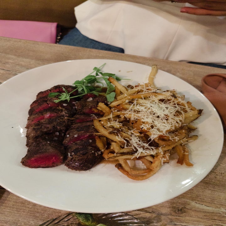 A plate of sliced steak with a garnish next to fries topped with shredded cheese