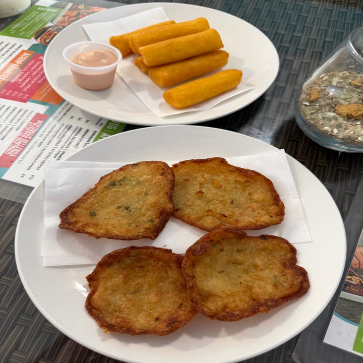 Two plates of food: one with crispy fried snacks and dip, the other with golden-brown fritters on a woven table surface