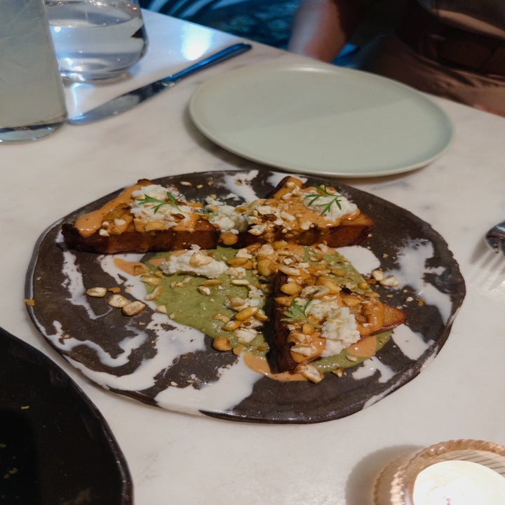 Gourmet dish featuring artisanal toast topped with ricotta cheese, herbs, and chopped nuts on a stylish plate