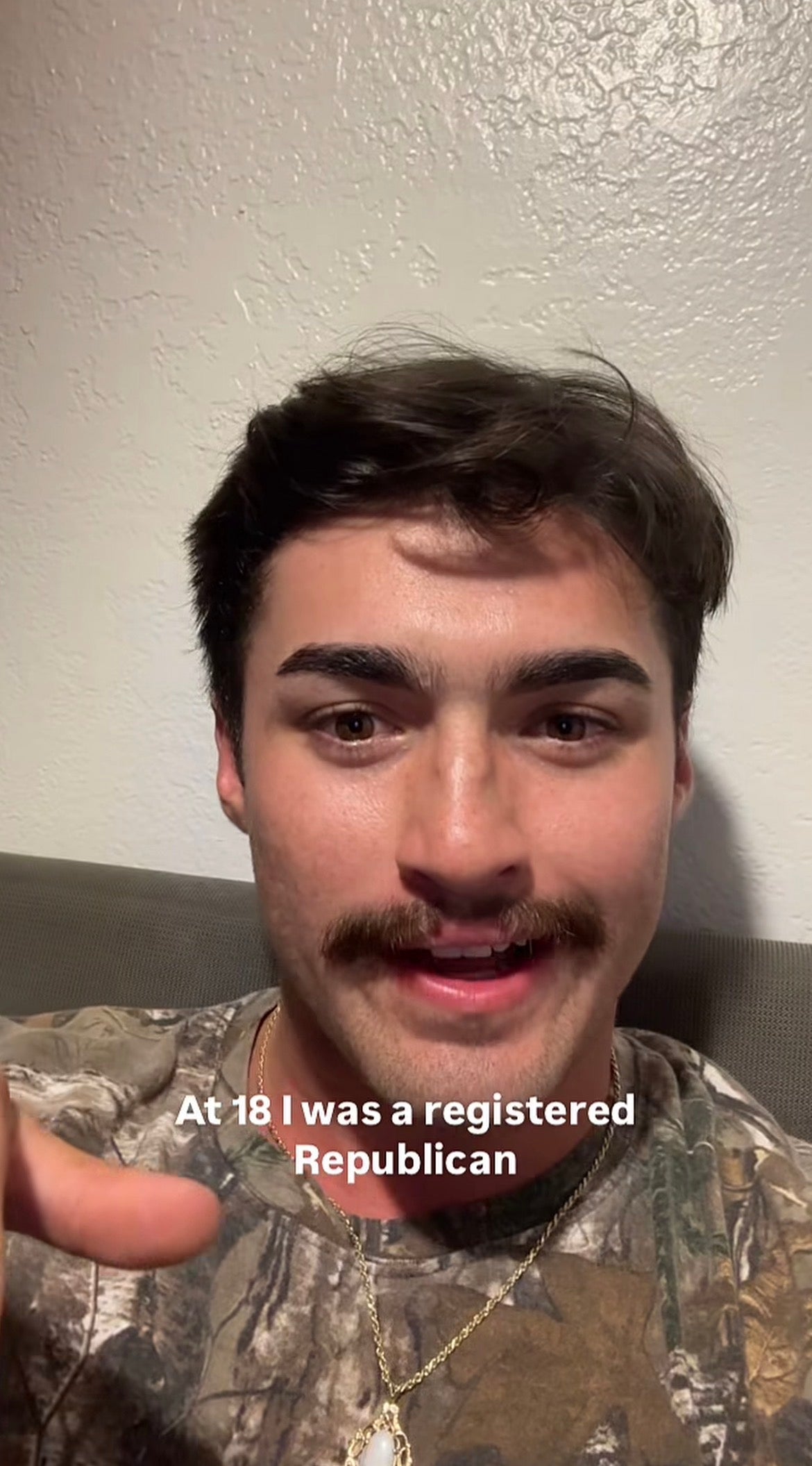 Person with a mustache, wearing a camo shirt, pointing at the camera; text reads, "At 18 I was a registered Republican."