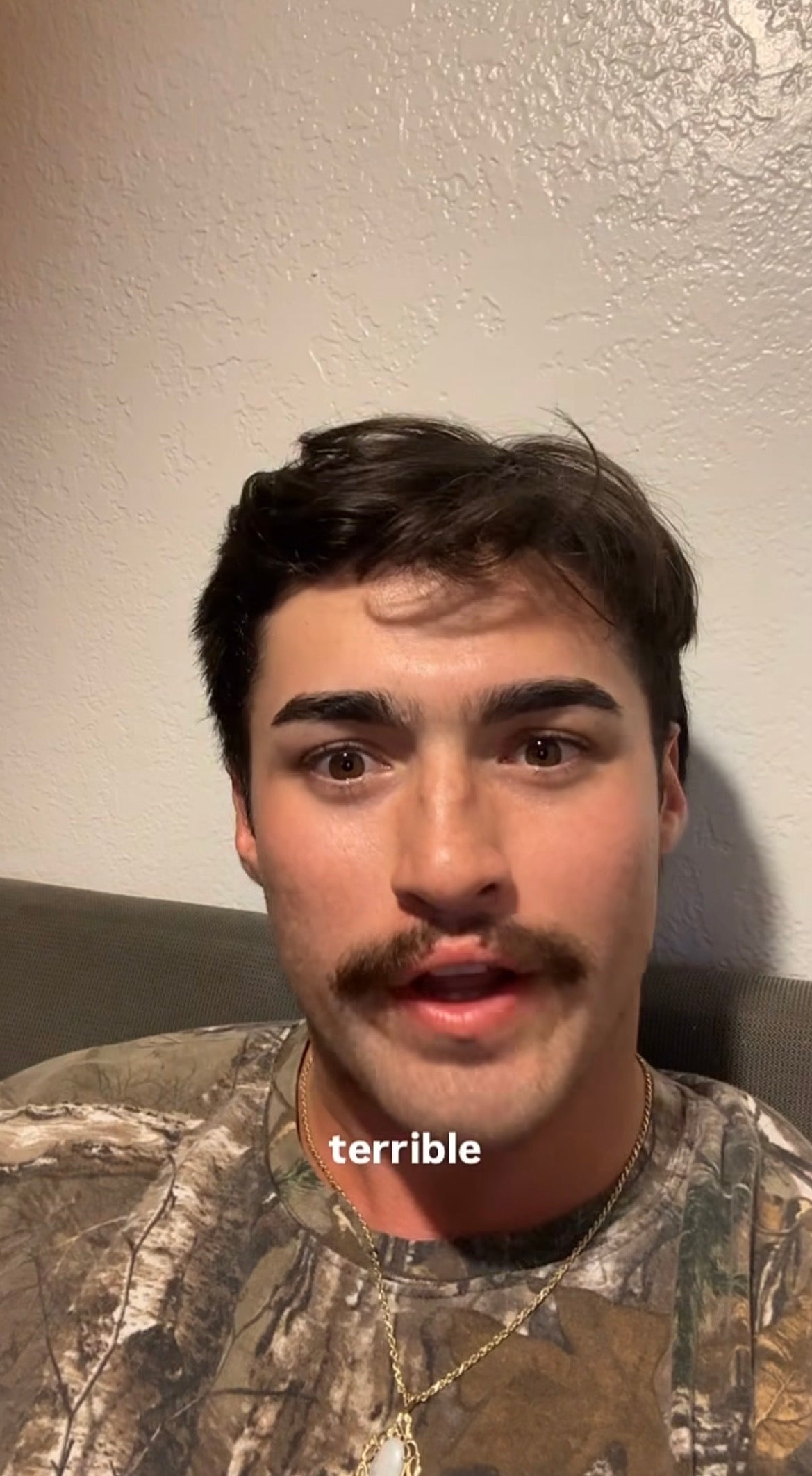 A person with a mustache is speaking to the camera while sitting on a couch. The text "terrible" appears on the image
