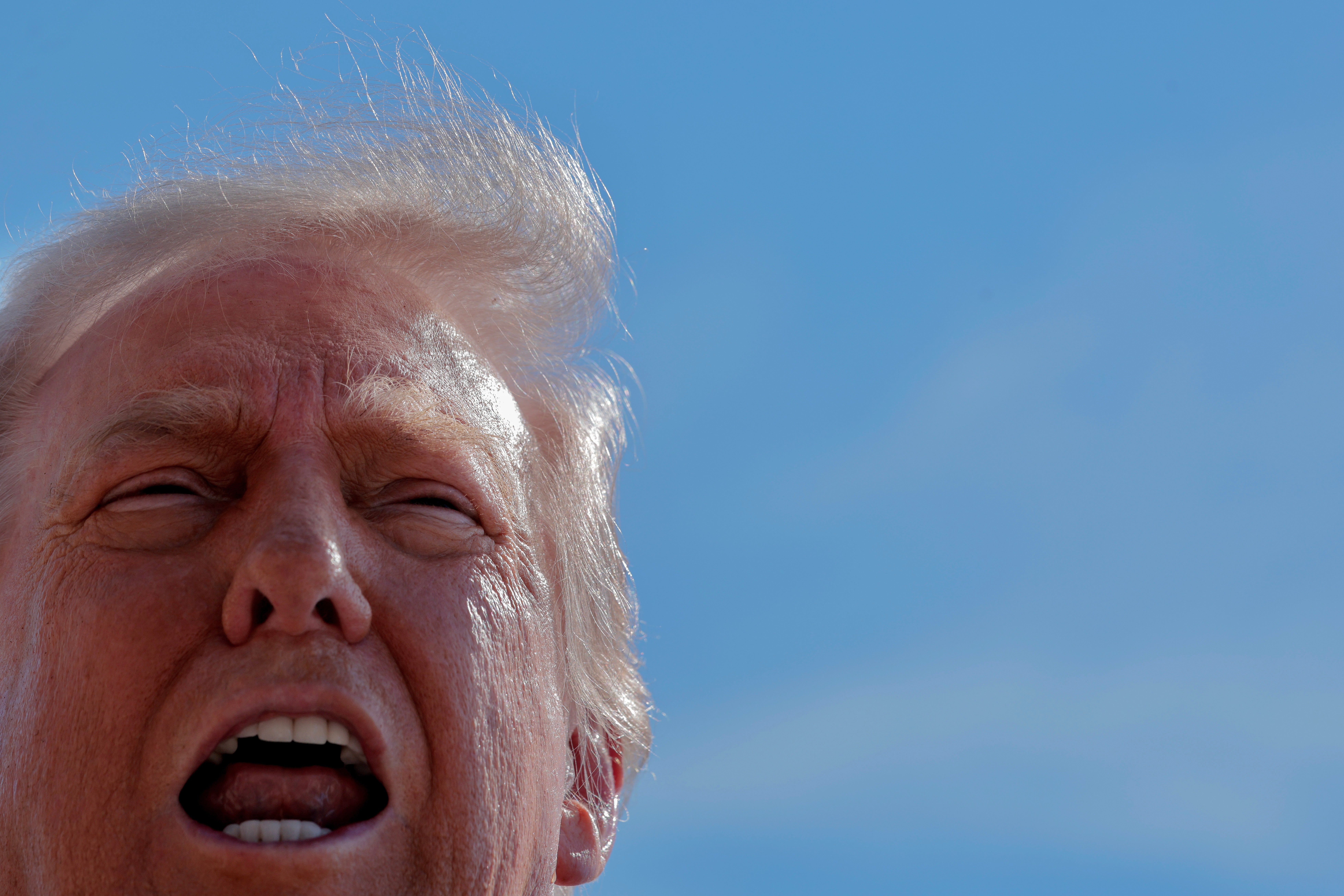 A person with wind-swept hair, mouth open, against a blue sky background