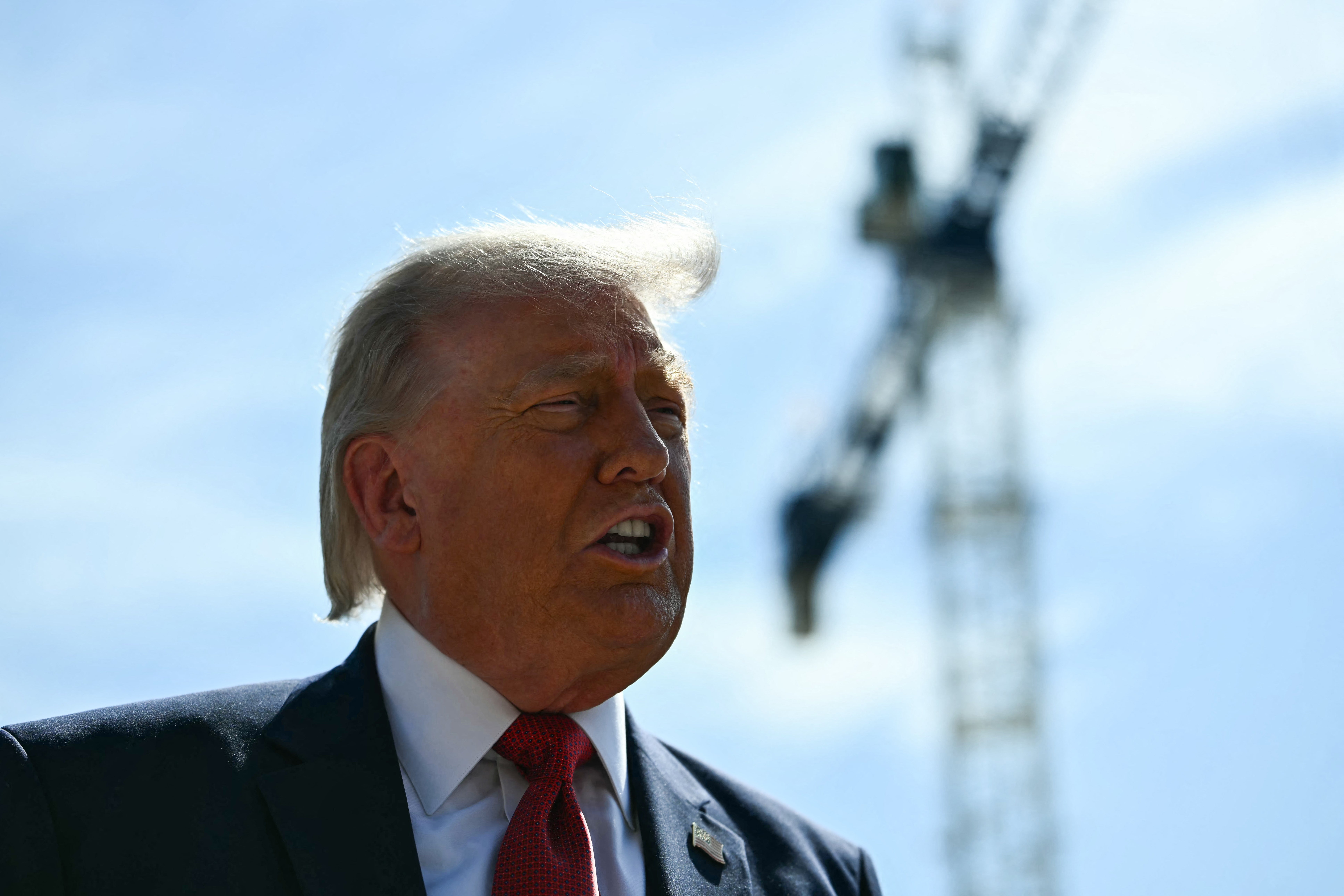 A person in a suit speaks outdoors with a construction crane in the background