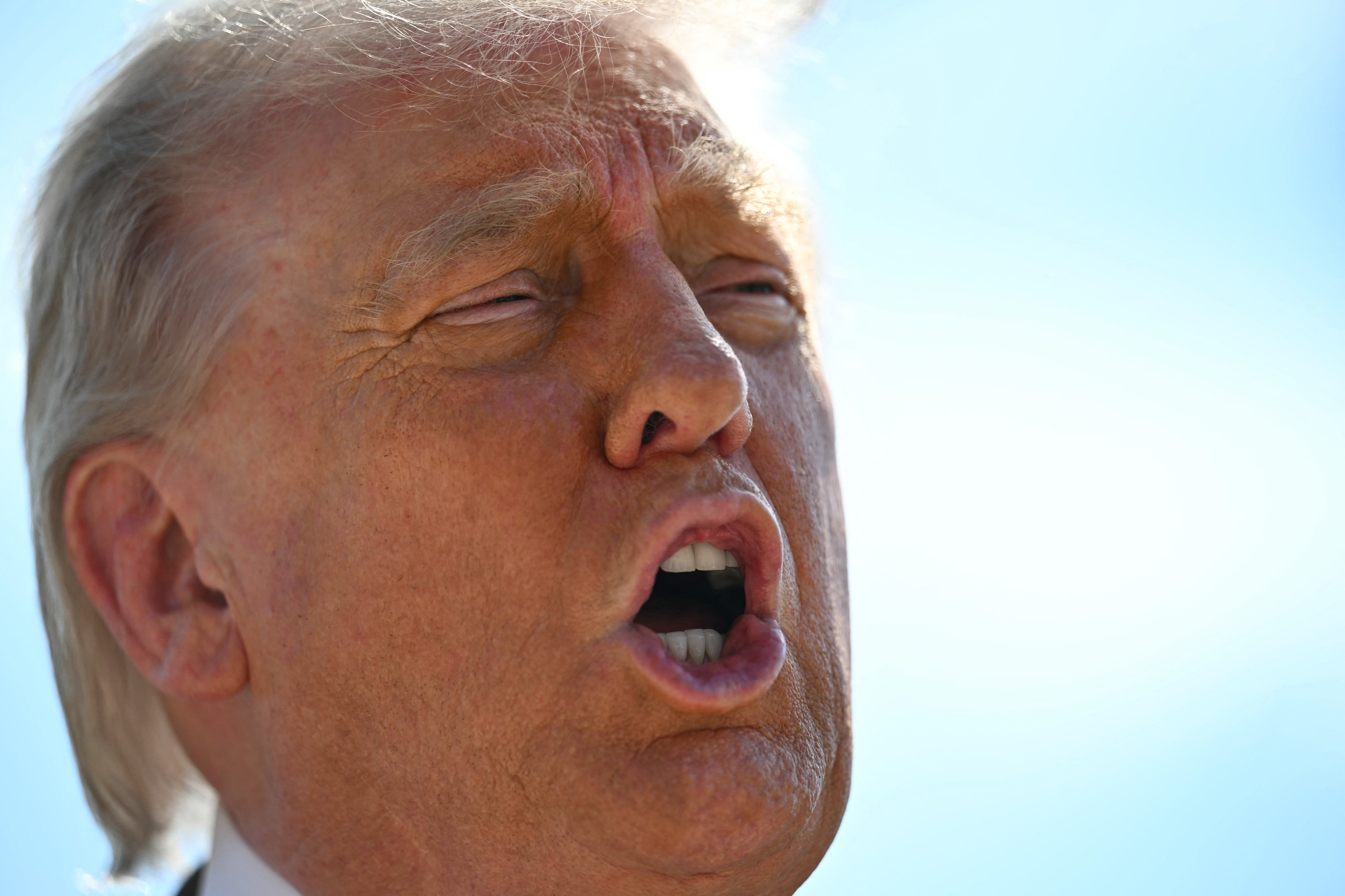A person with a light-colored suit appears to be speaking passionately outdoors