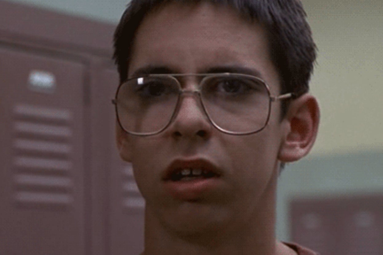 A person with glasses is standing in front of lockers, looking surprised or confused