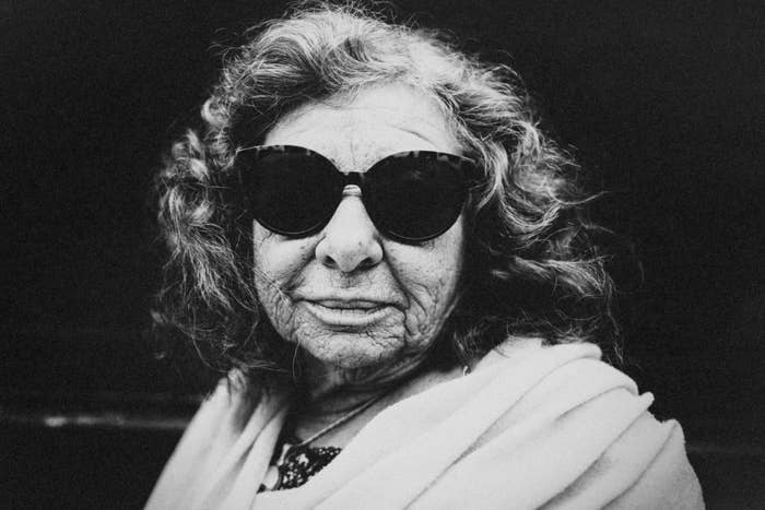 Older woman wearing large sunglasses, looking directly at the camera with a neutral expression