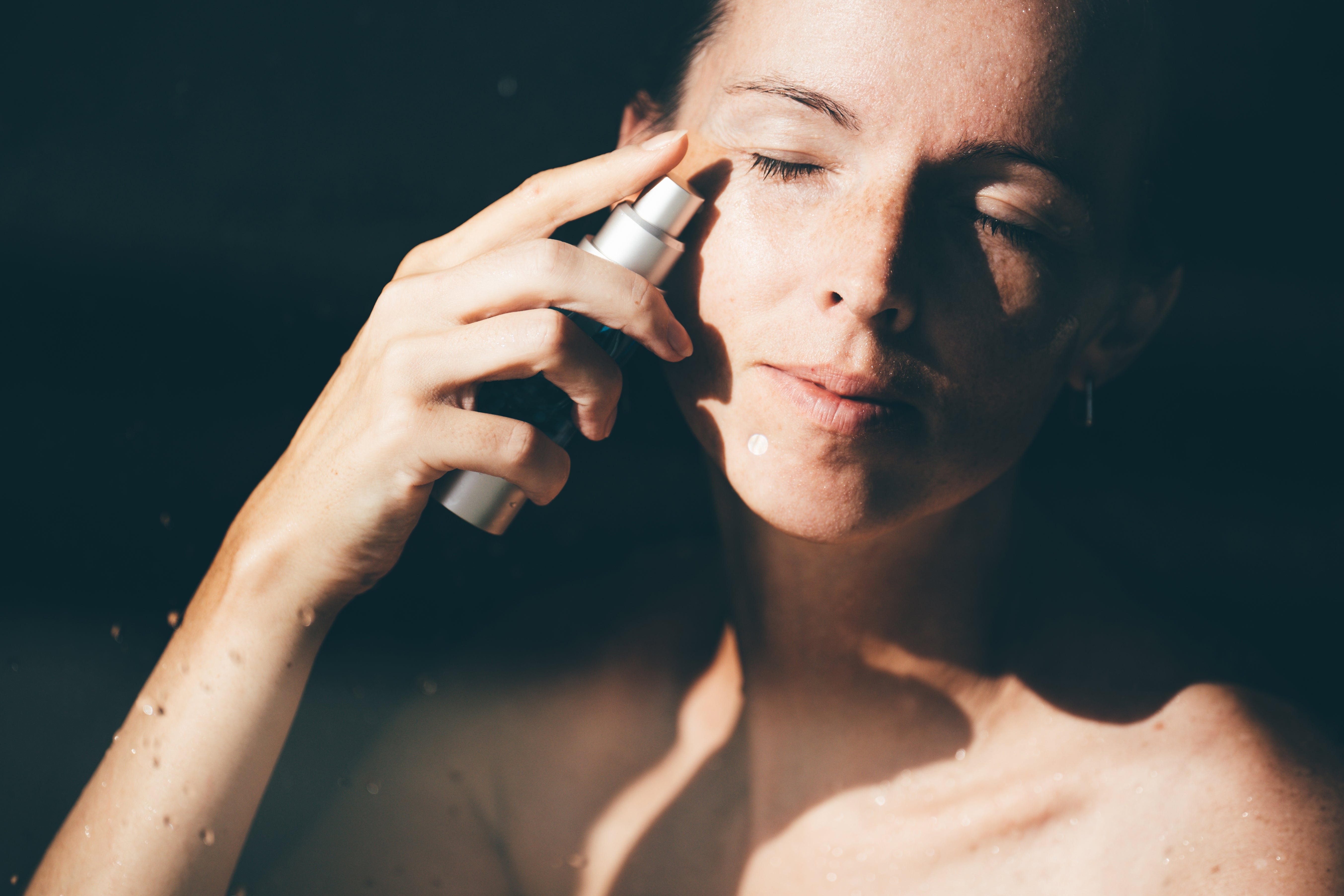 Person applying skincare product to face with closed eyes, emphasizing self-care or skincare routine
