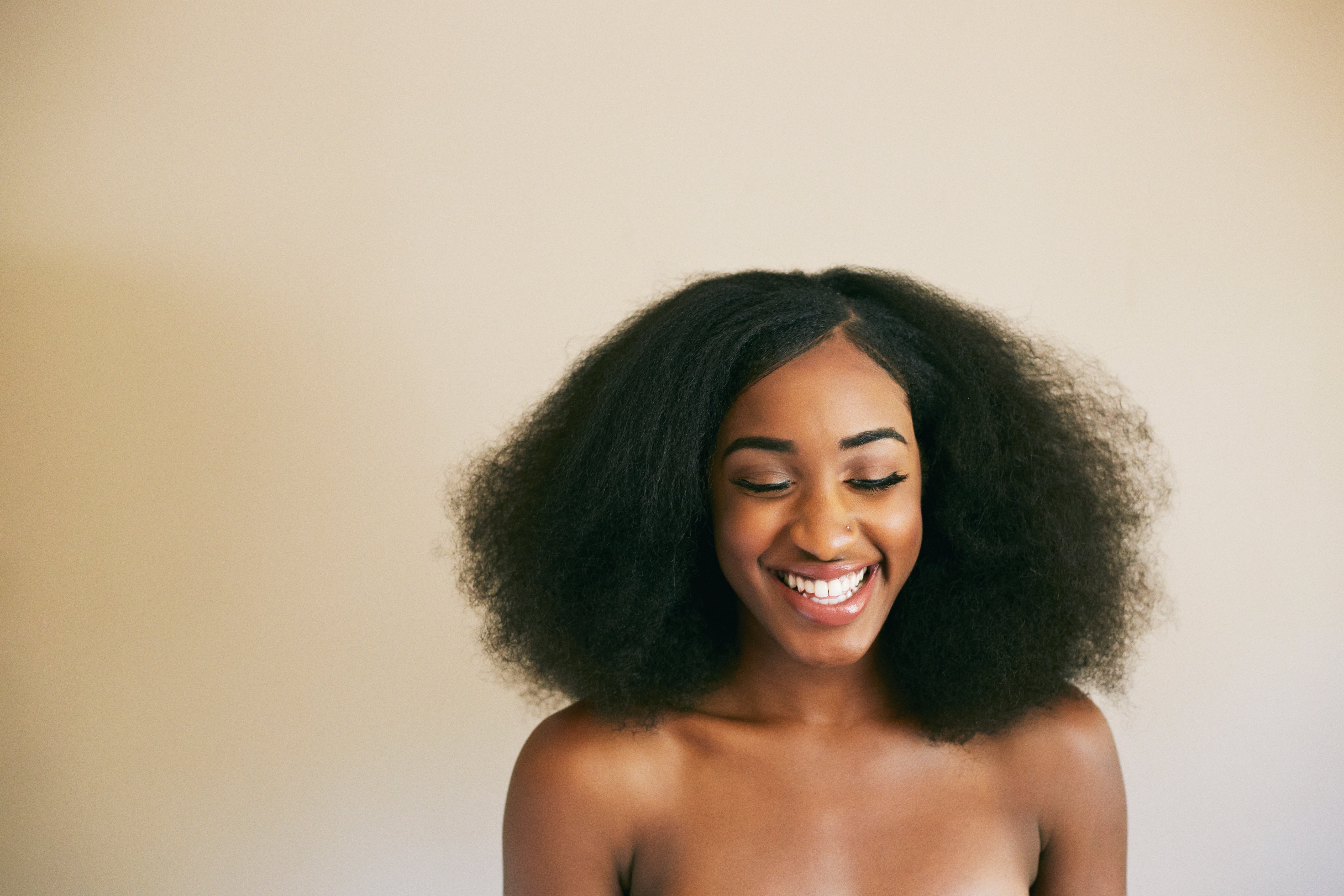 Person smiling warmly with eyes closed, showcasing natural curly hair. The image evokes a sense of joy and serenity
