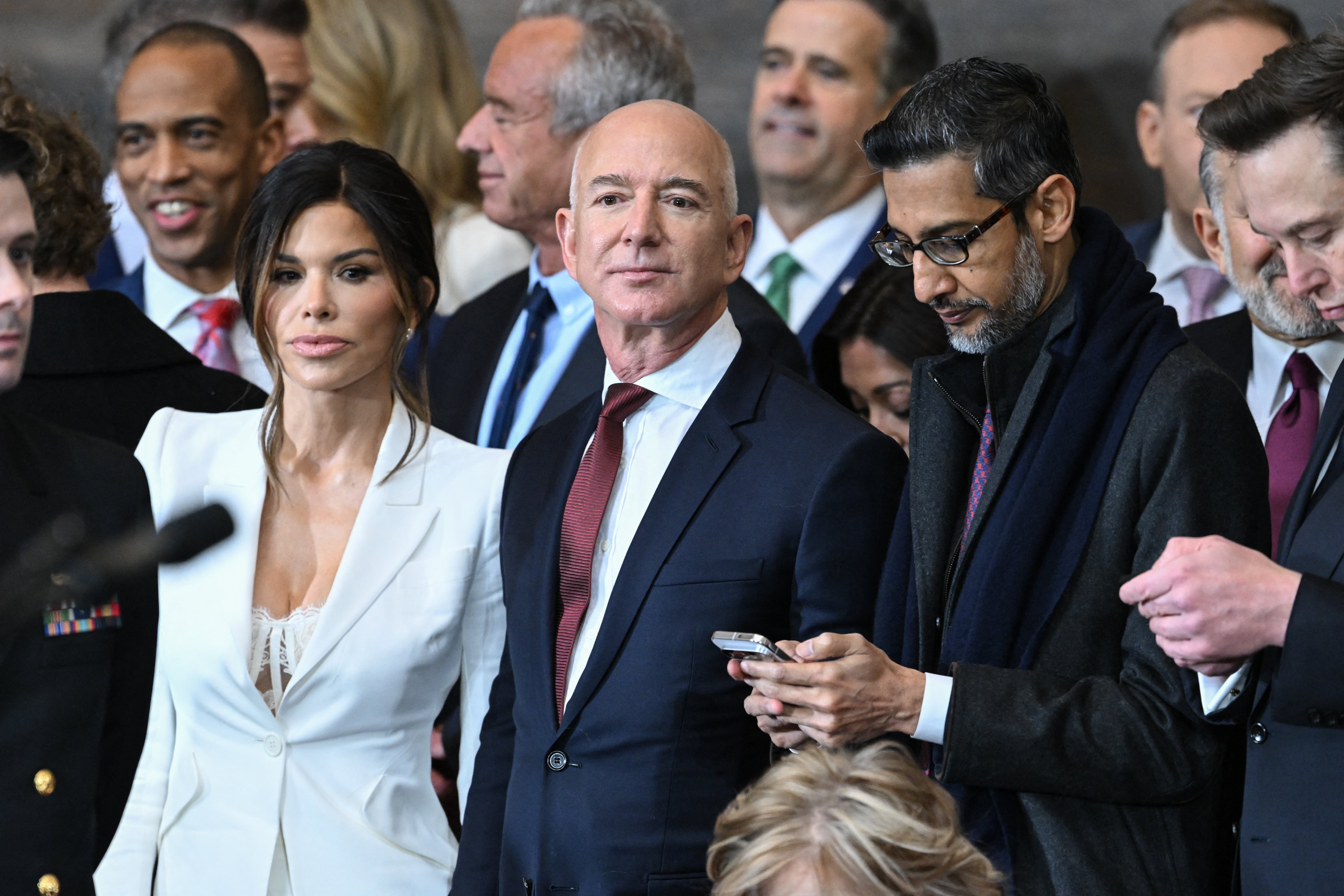 A group of well-dressed individuals, including a woman in a white suit and two men in formal attire, are standing together at an event