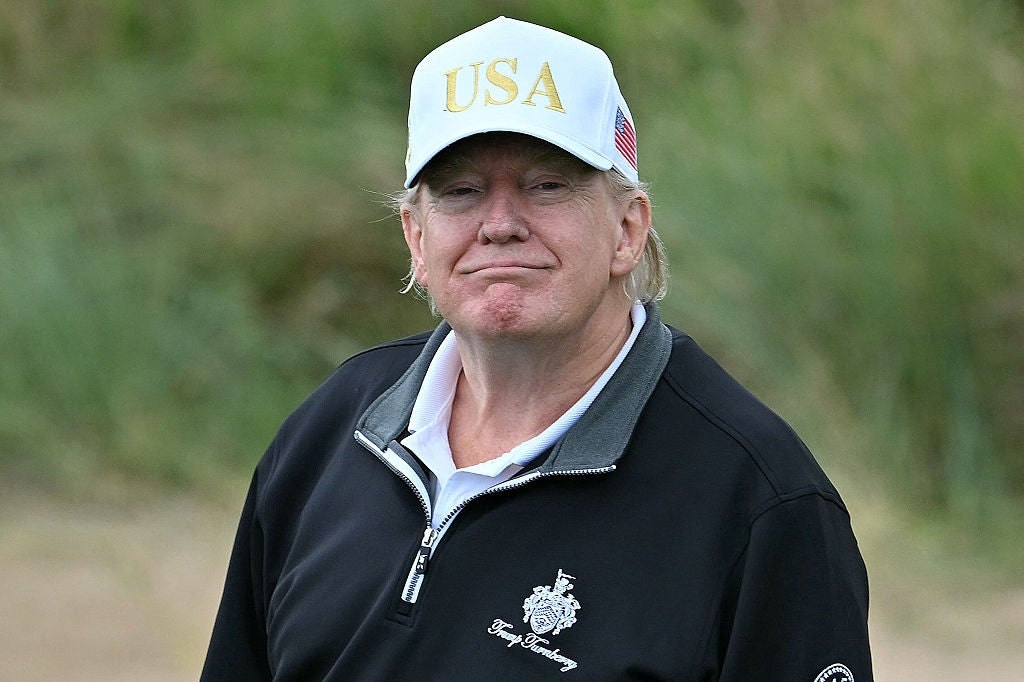 Man wearing a "USA" cap and casual sporty jacket with emblem, smiling slightly outdoors