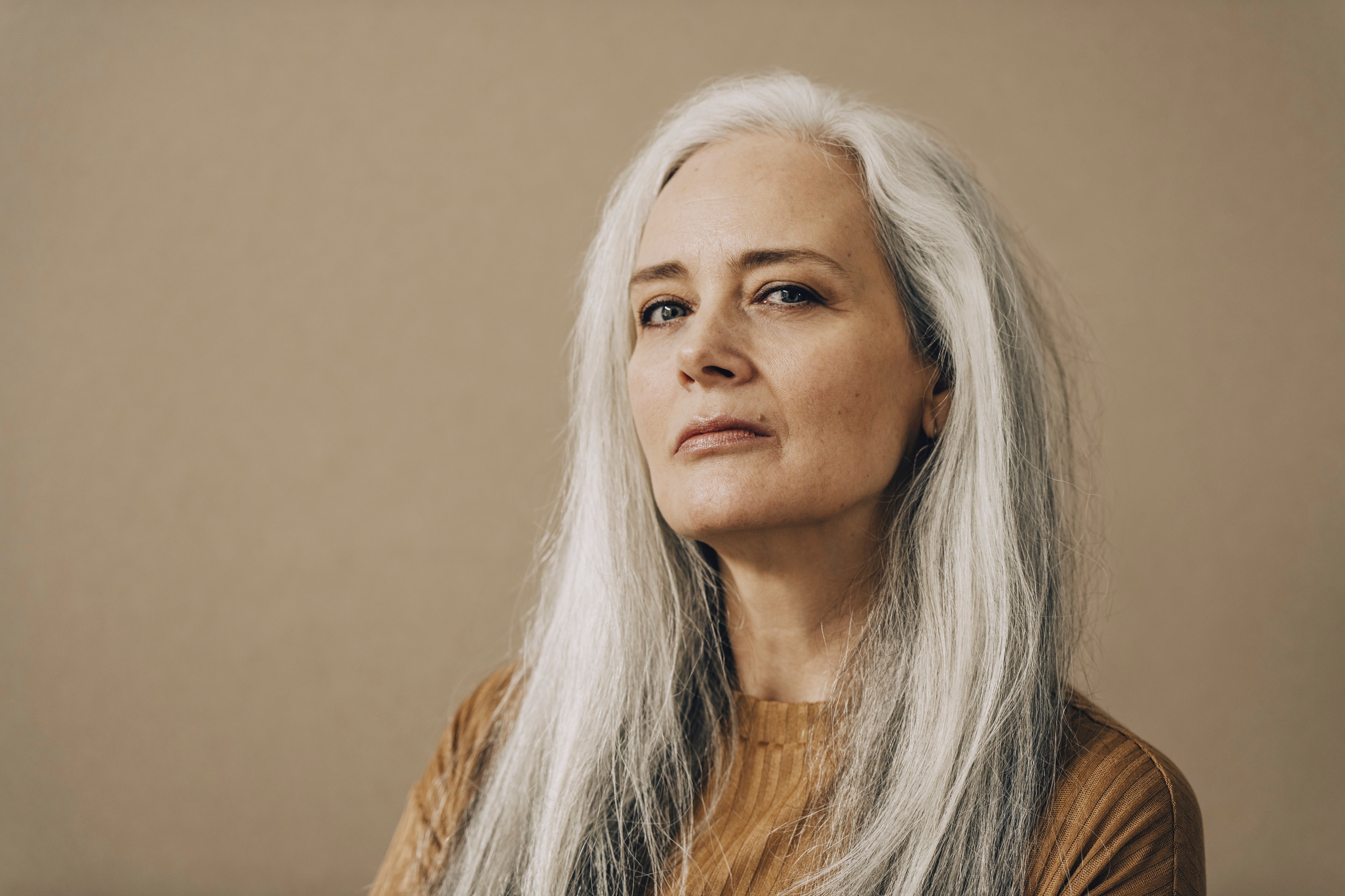 Woman with long gray hair and a confident expression poses against a neutral background