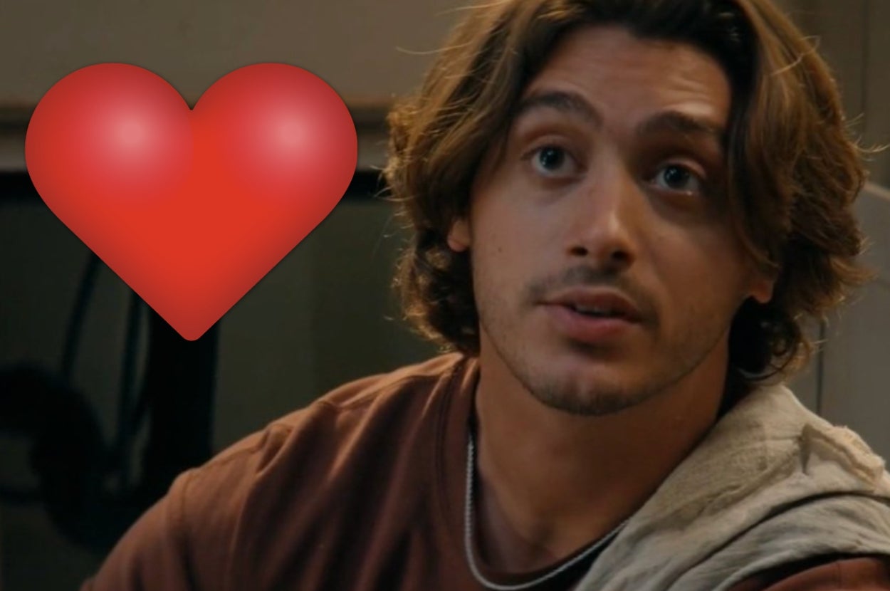 Person with medium-length hair and a casual outfit, sitting indoors with a large red heart emoji beside them