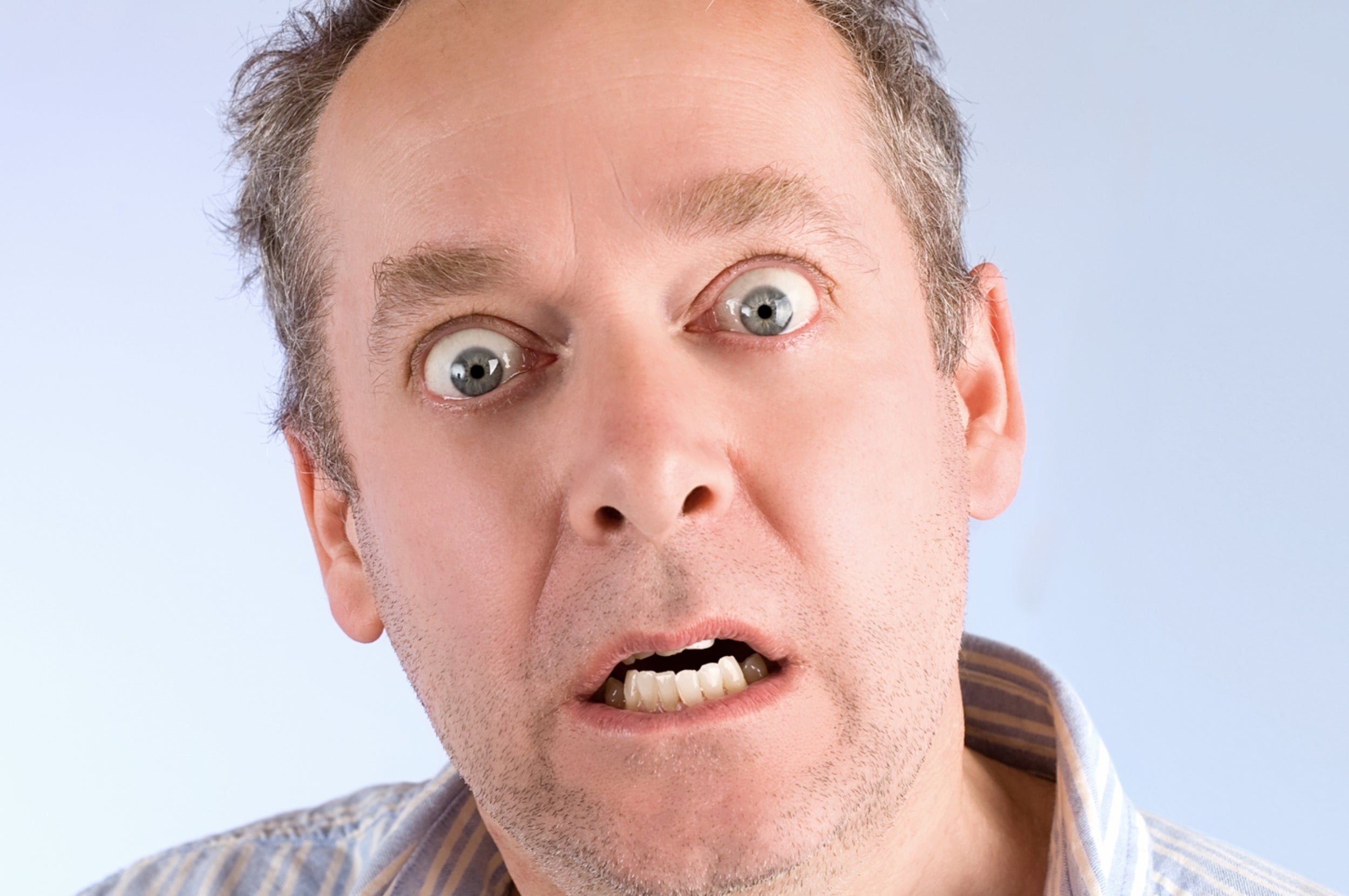 A surprised person with wide eyes and mouth open, wearing a striped shirt, poses against a plain background
