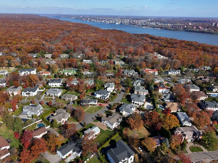 Aerial presumption    of a suburban vicinity  with galore   houses surrounded by autumn trees, adjacent  to a wide   stream  and cityscape successful  the distance