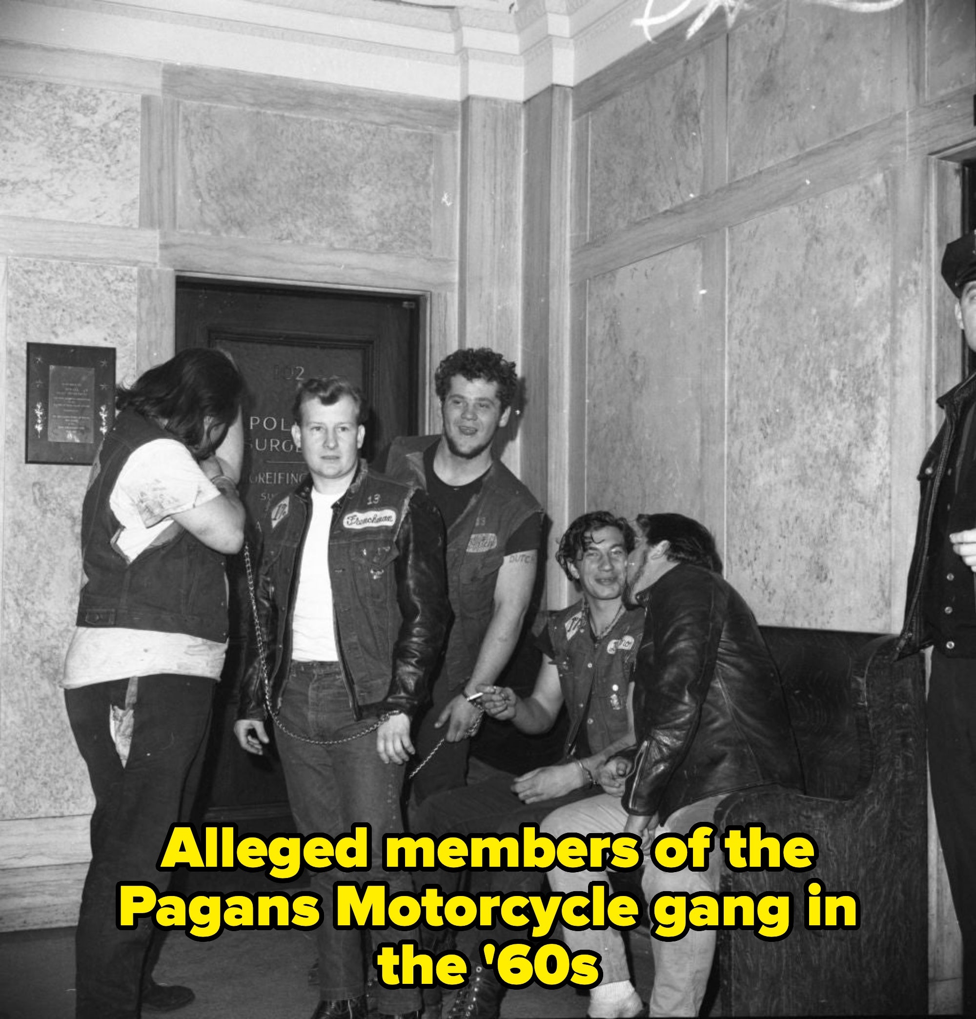 A radical  of men successful  leather jackets with patches are successful  a room, talking and smiling. One leans against the wall, portion    others beryllium   and basal   close