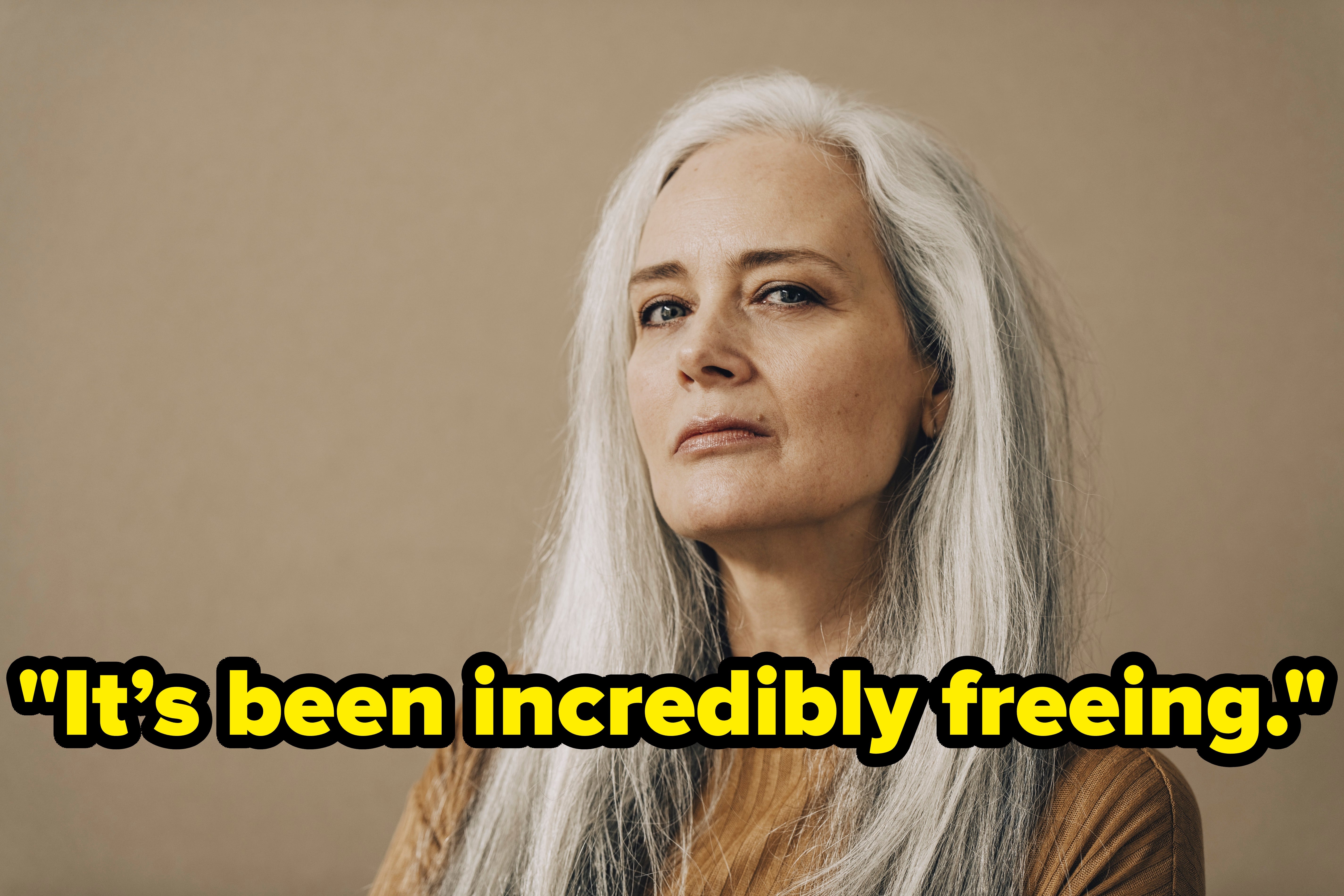 Woman with long gray hair and a confident expression poses against a neutral background