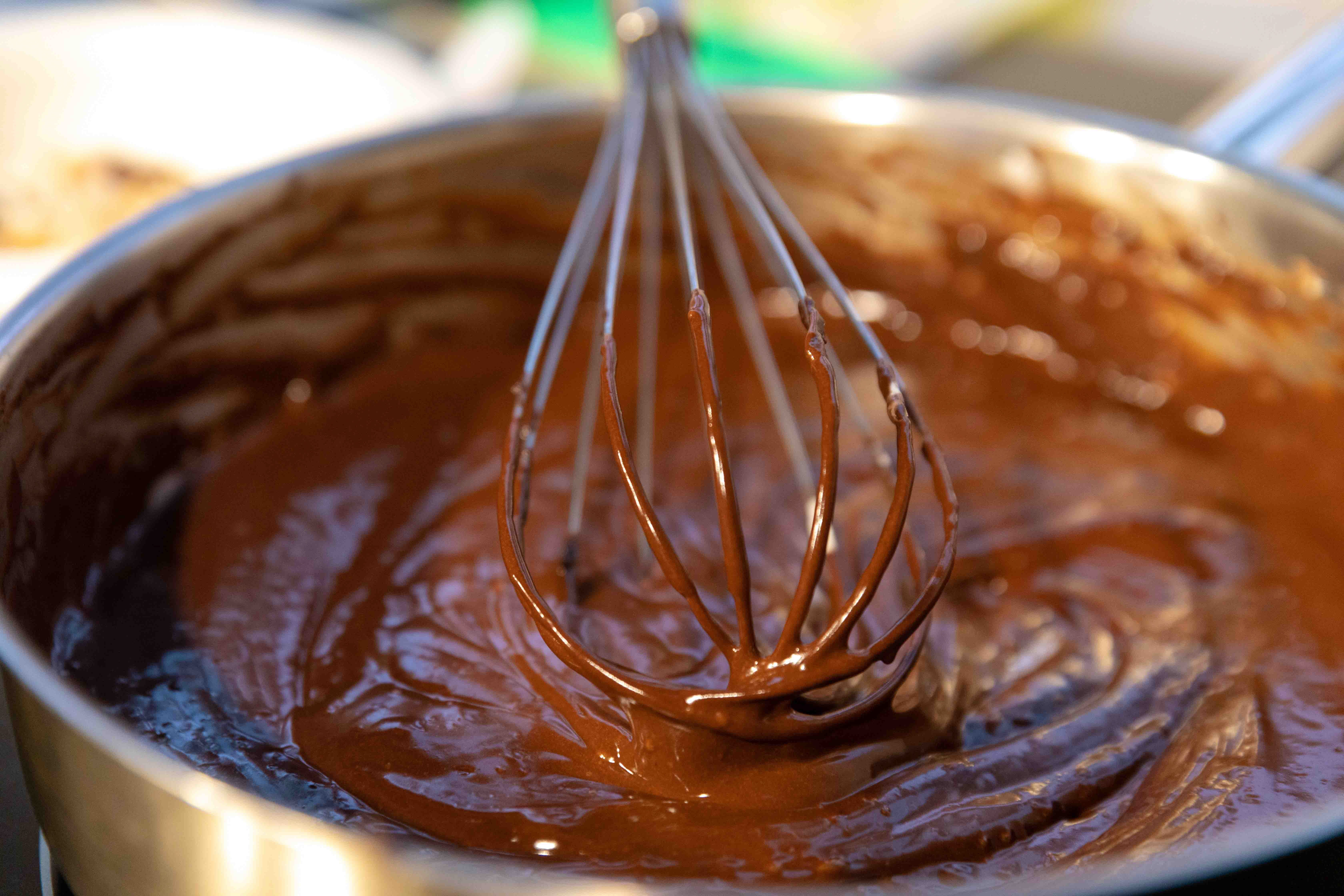 A whisk mixes smooth chocolate batter in a metal bowl, highlighting a cooking preparation process