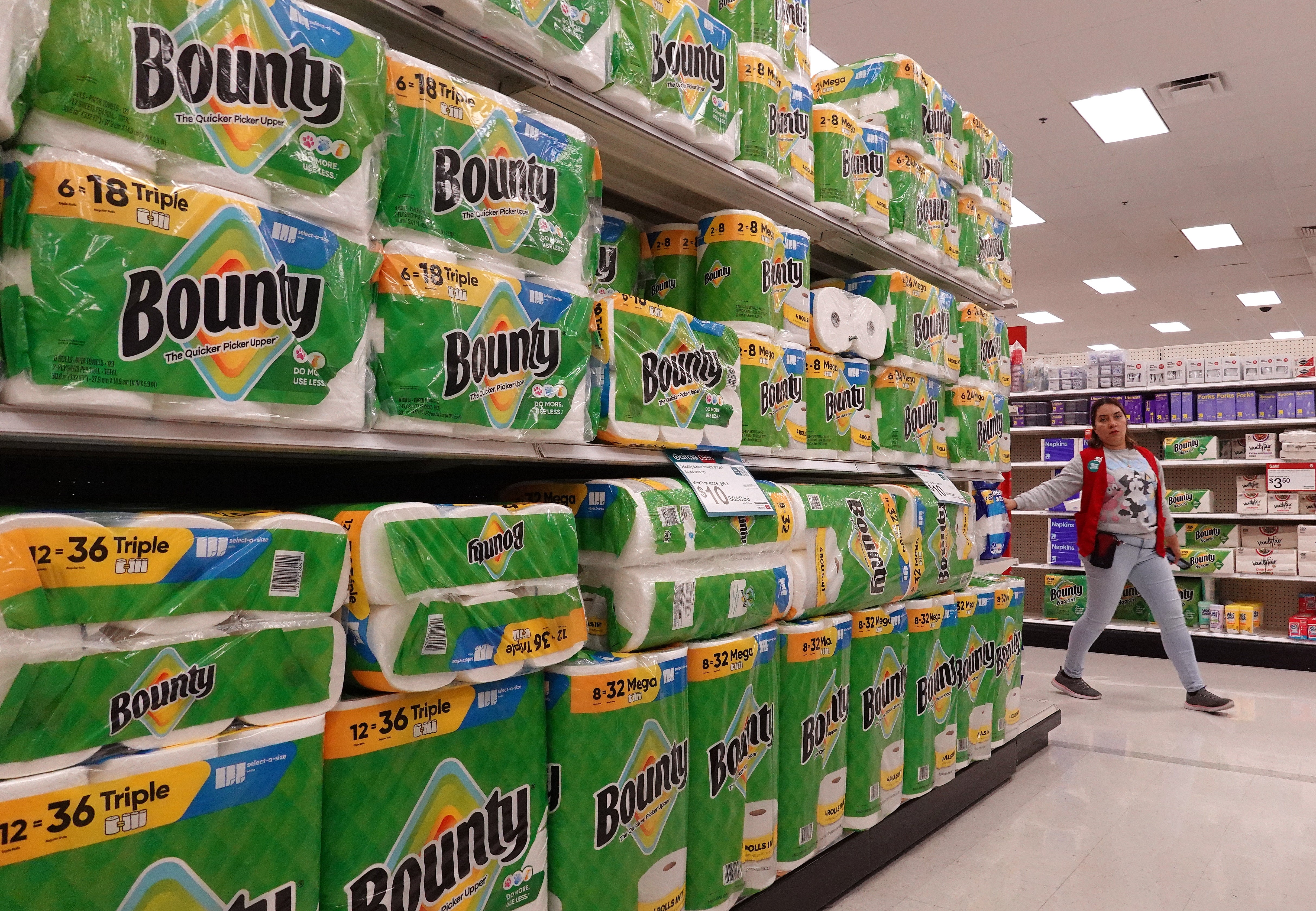 A person stands near stacked shelves filled with packs of Bounty paper towels in a store aisle