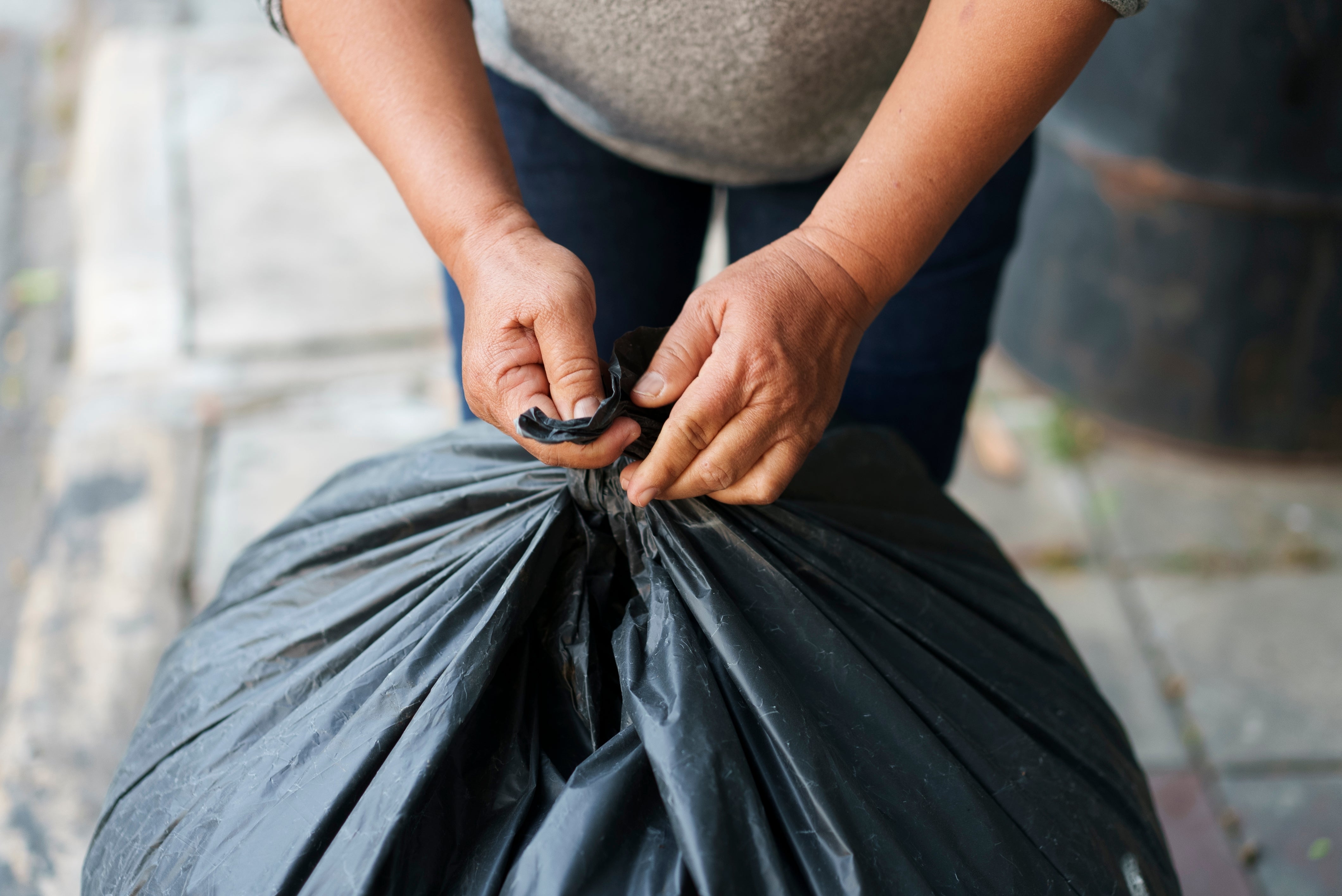 Person tying a garbage bag tightly outdoors, focusing on hands and the top of the bag