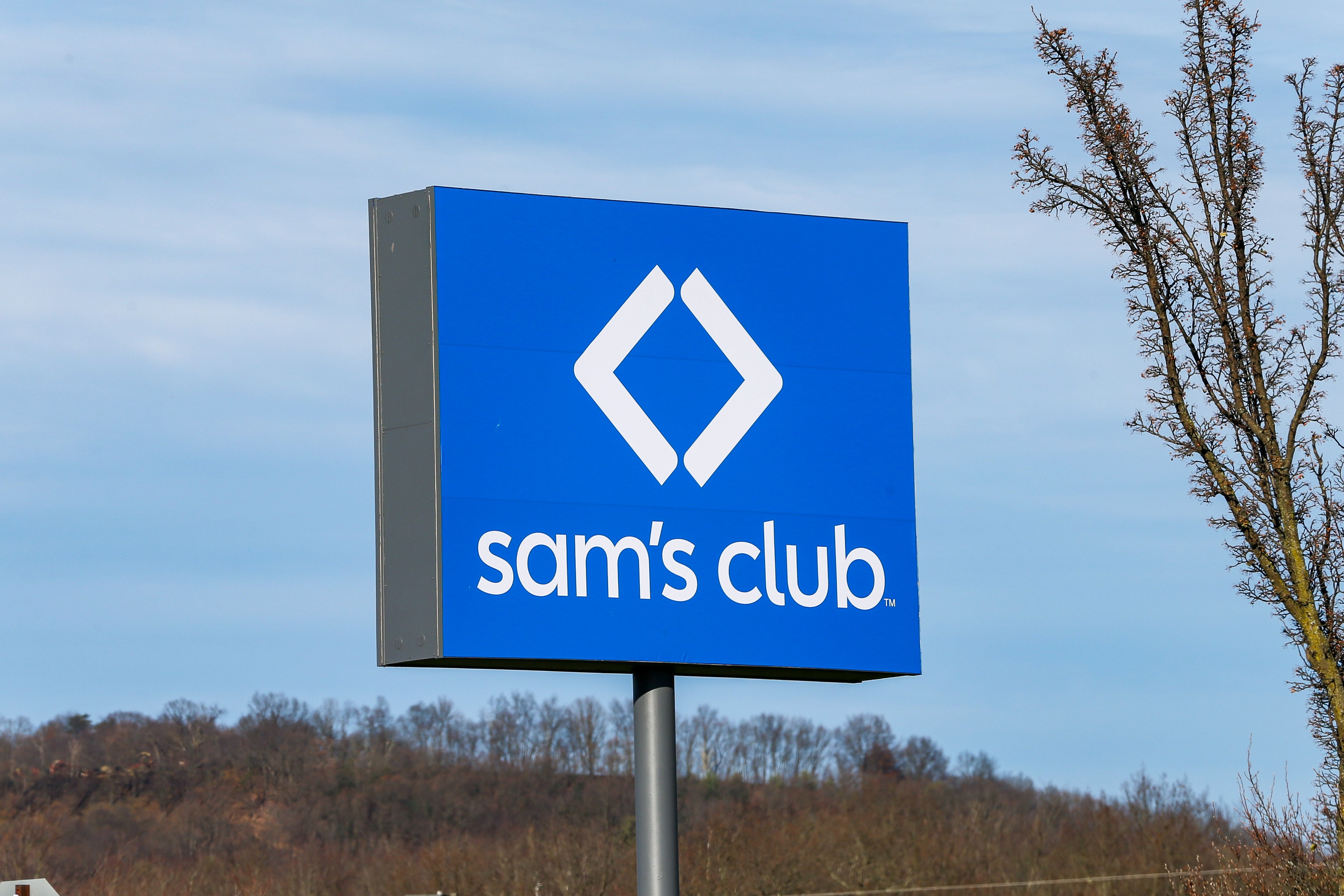 Sam's Club sign with a logo featuring a diamond shape, set against a backdrop of trees and sky