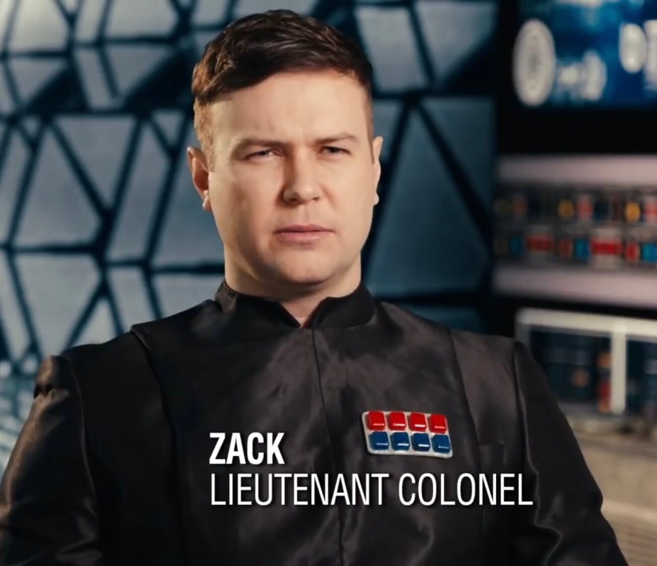 A man identified as Lieutenant Colonel Zack wears a dark uniform with colorful badges, set against a futuristic, geometric background