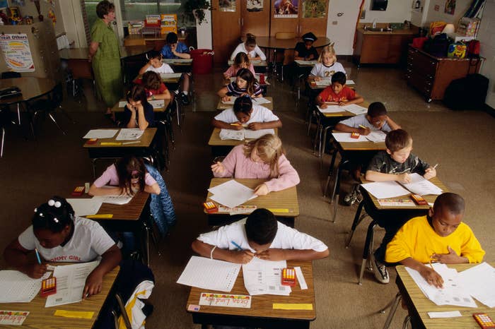 Children sitting astatine  desks successful  a classroom, focused connected  penning  and drafting  activities, with a teacher   observing