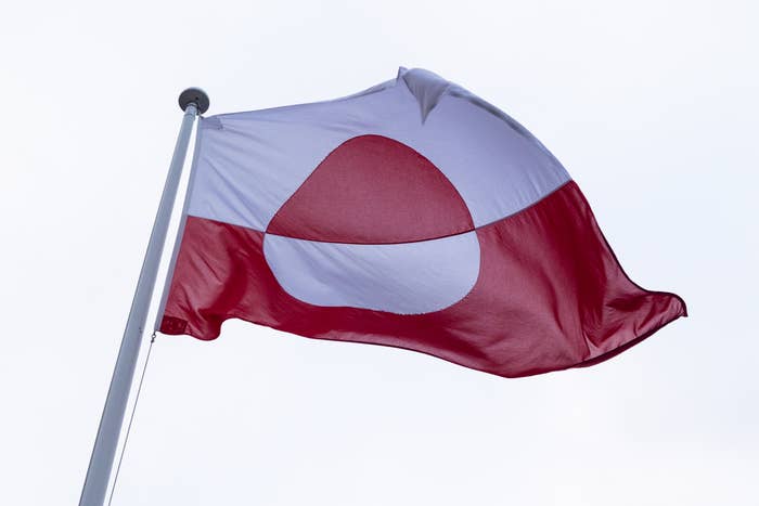 Flag of Greenland with a large white circle partially overlapping a red background, waving on a flagpole against a clear sky
