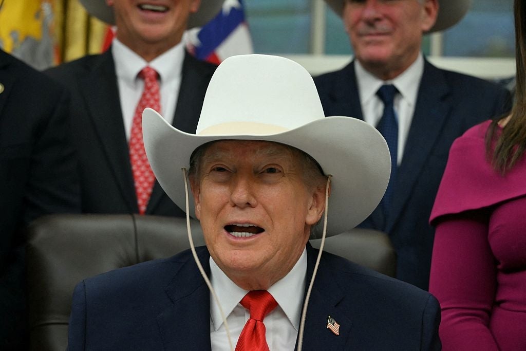 Man wearing a cowboy hat and suit speaks while seated, surrounded by others in similar attire