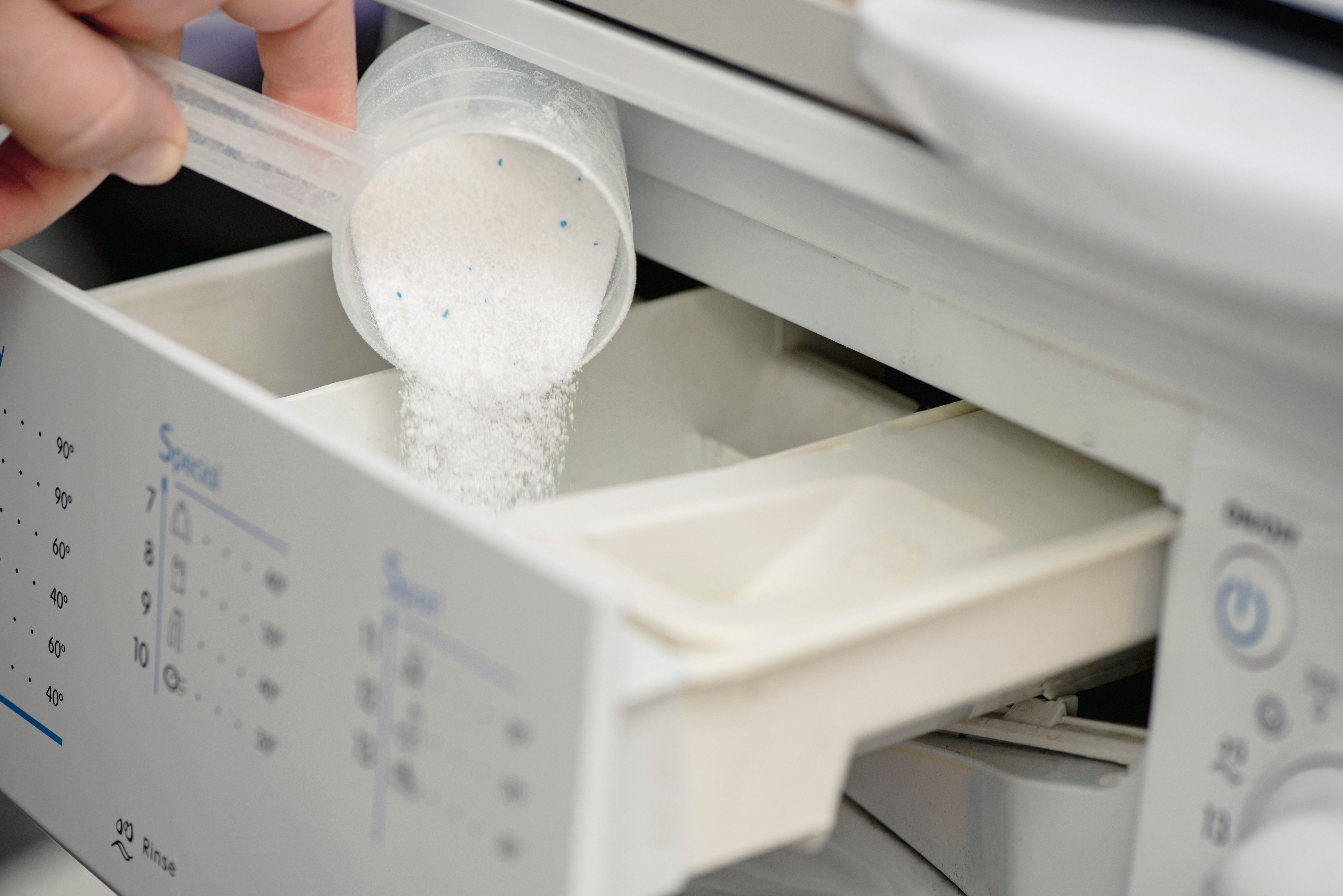 Pouring detergent powder into a washing machine drawer, focusing on home appliance use