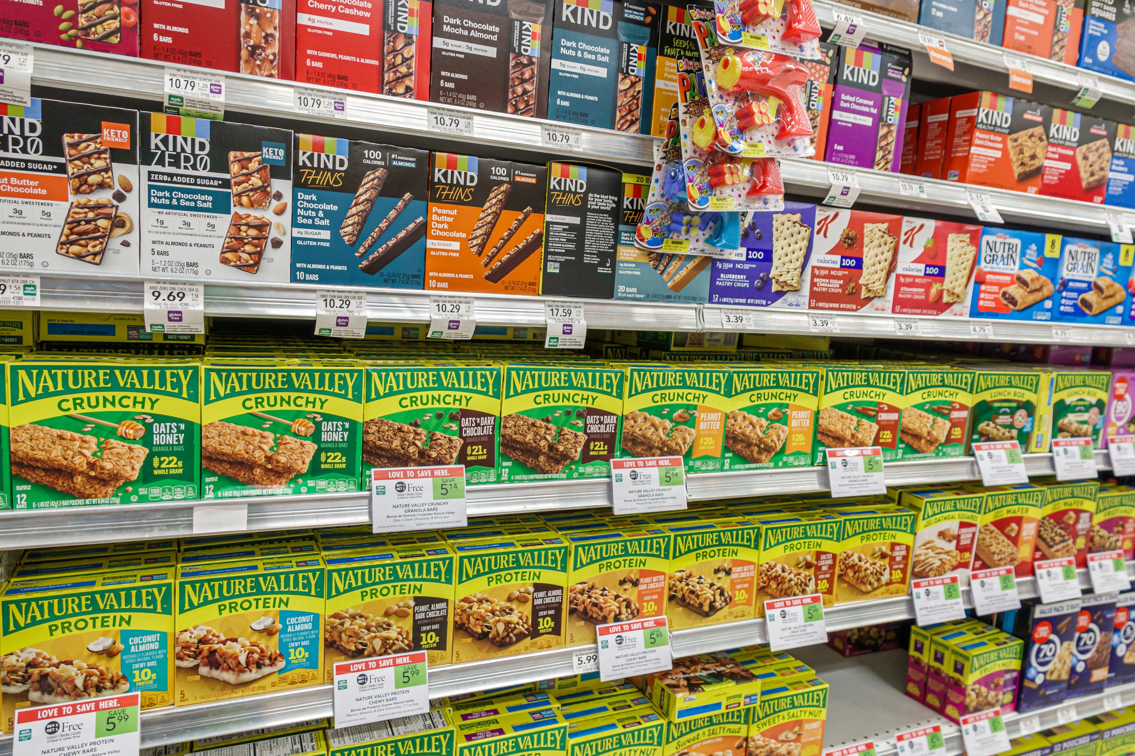 Store shelves stocked with various brands of granola bars, including Nature Valley and Kind, showcasing product variety and prices
