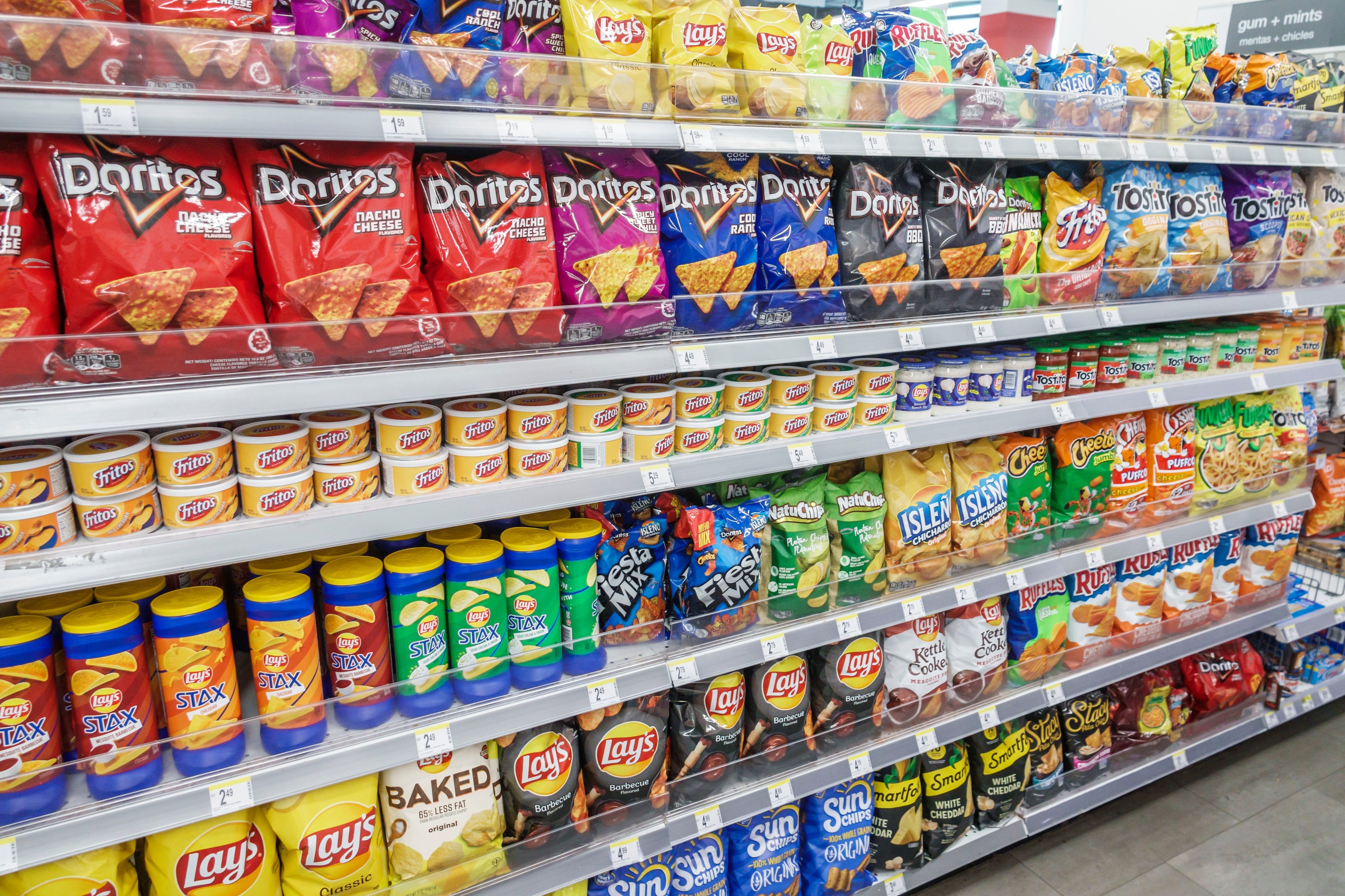 Store shelves filled with various brands of chips and snacks, including Doritos, Lay's, and Tostitos, neatly organized in rows