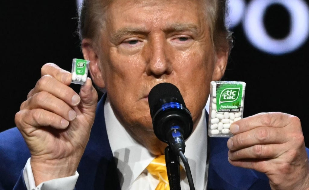 Person holding two packs of Tic Tac mints while speaking at a microphone