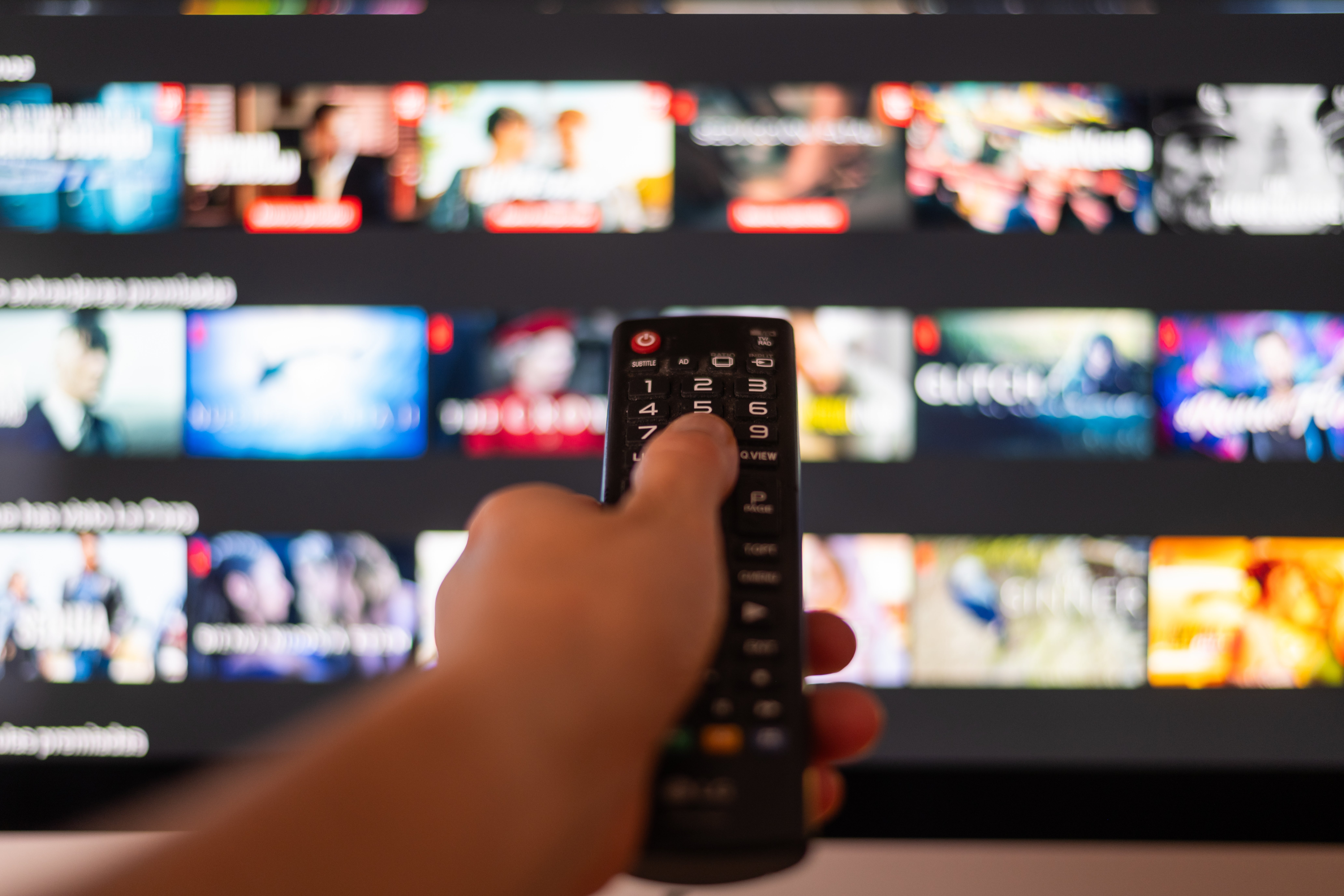 A hand holds a remote control, pointing at a streaming service menu on a TV screen, suggesting a choice for a romantic film night
