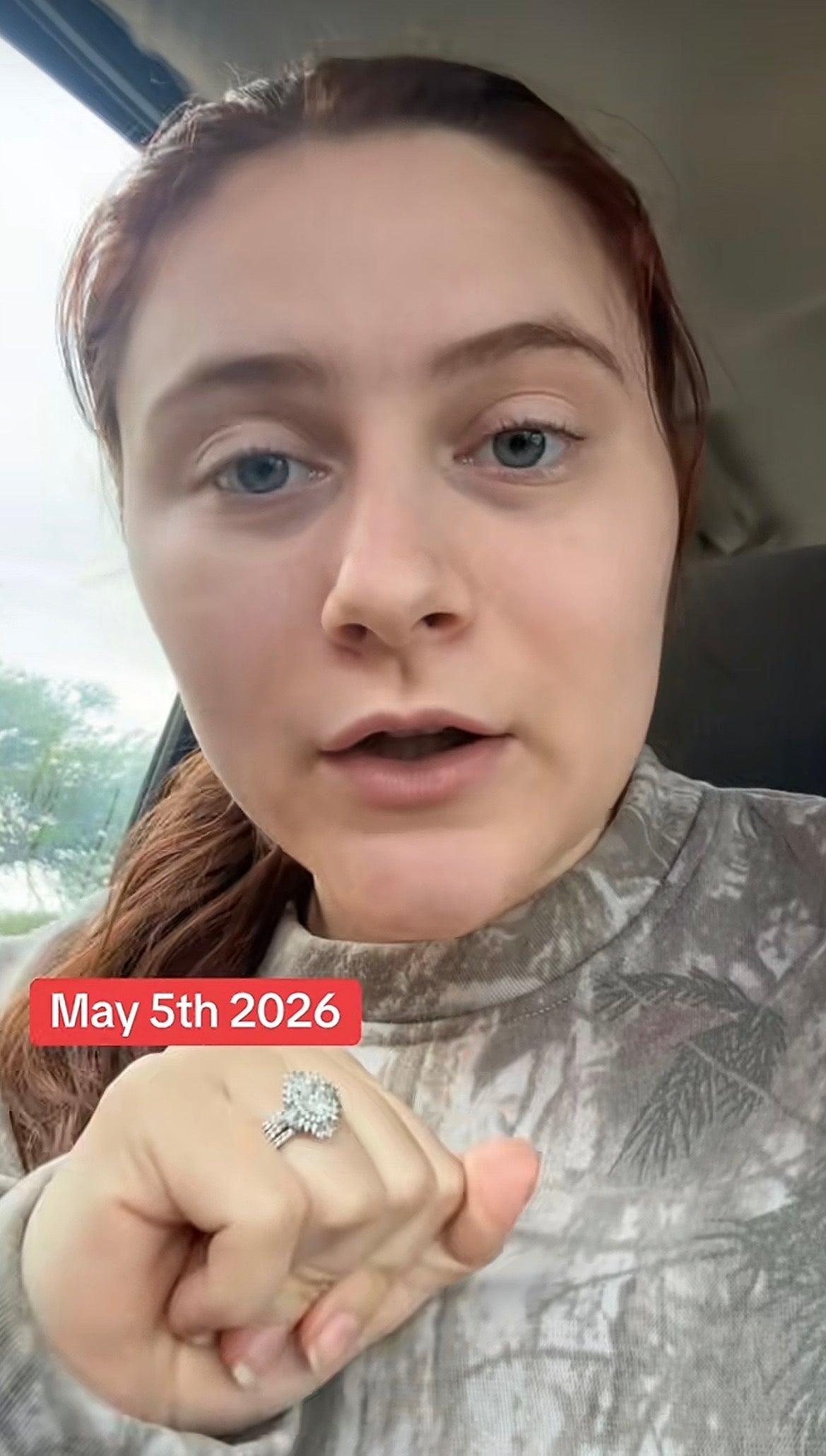 Person with long hair in car points to engagement ring. Date overlay reads May 5th, 2026