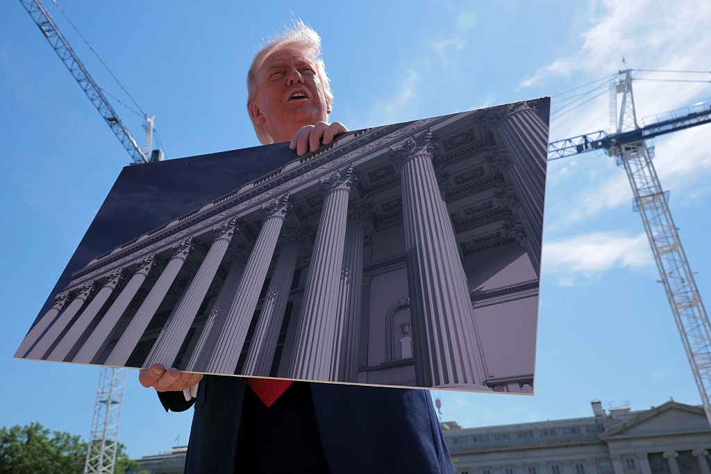 Person holding an architectural image of a building with columns, standing outdoors near construction cranes