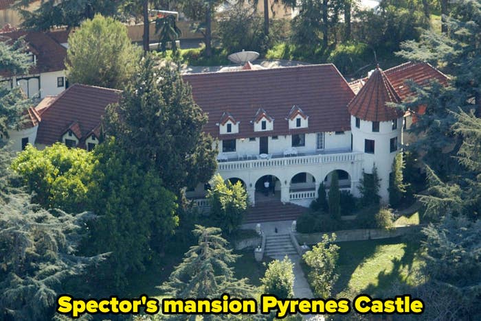 An aerial view of a large, historic mansion surrounded by trees, featuring a red-tiled roof and arched entryway