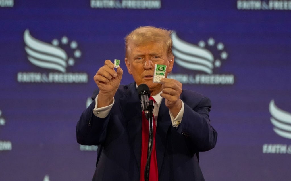 A man in a suit holds up two objects at a podium during a speech
