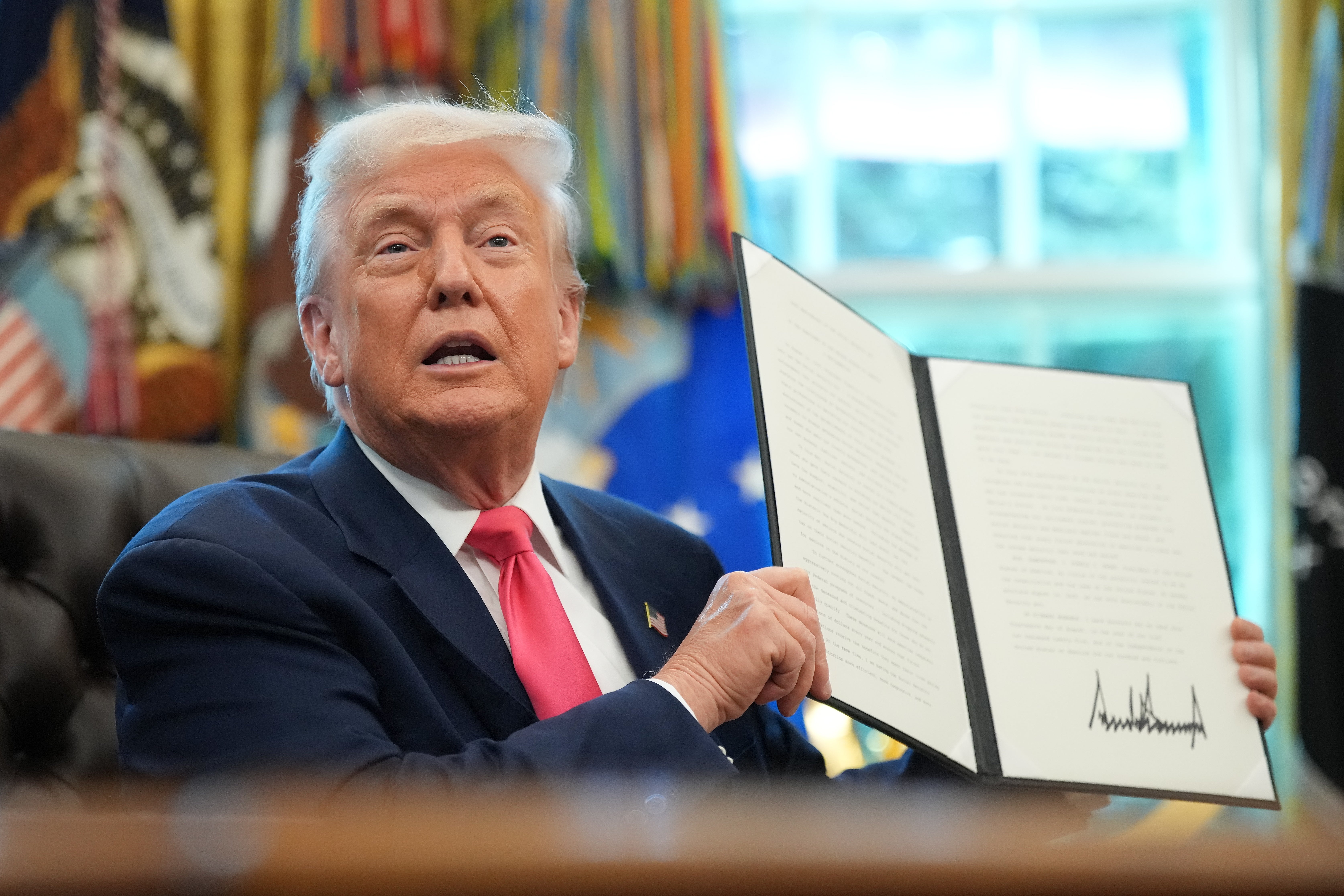 A person holding a signed document in a formal setting, appearing to present it to an audience